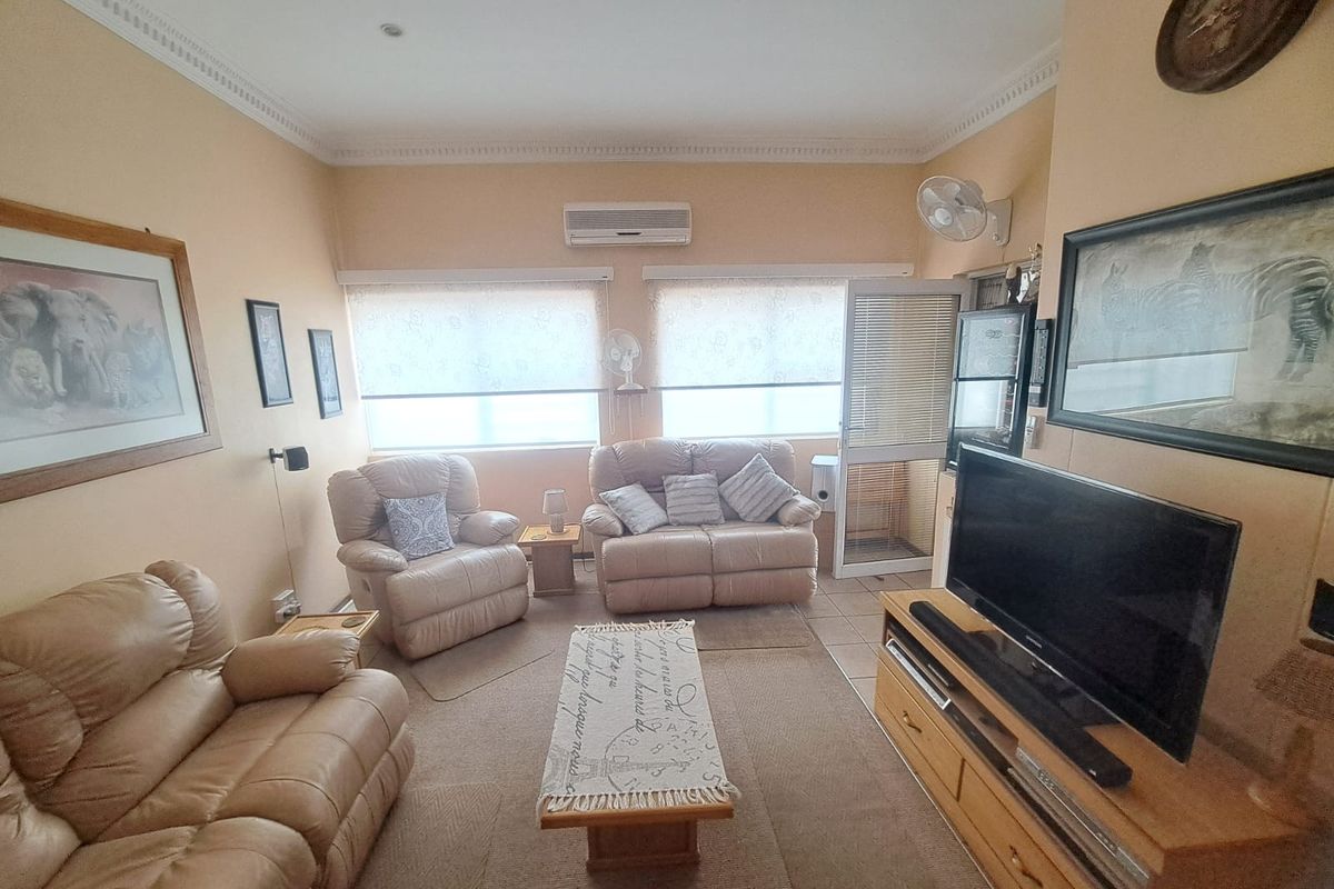 A comfortable living room featuring tiled flooring, decorative cornice, and a wall-mounted split-system air conditioner with natural light from dual windows.