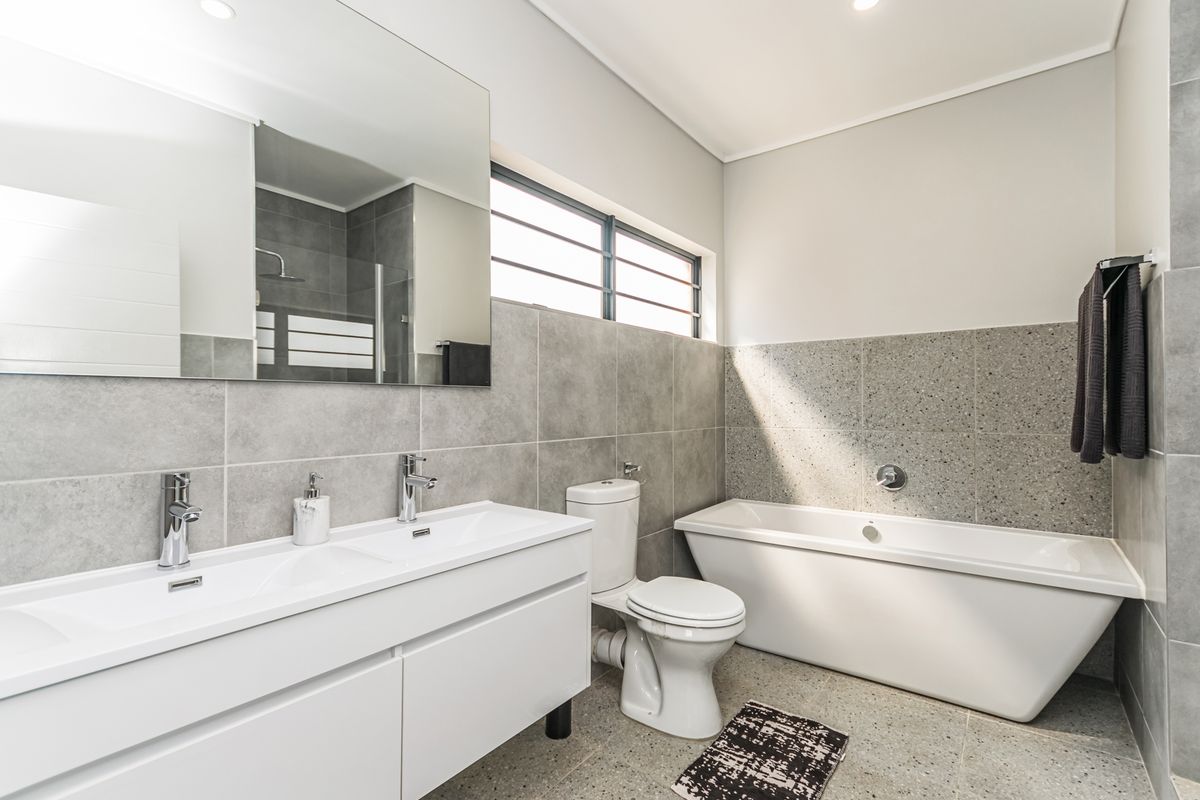 Modern bathroom featuring a double vanity, freestanding bathtub, and contemporary grey tiling with high-quality finishes and natural light.