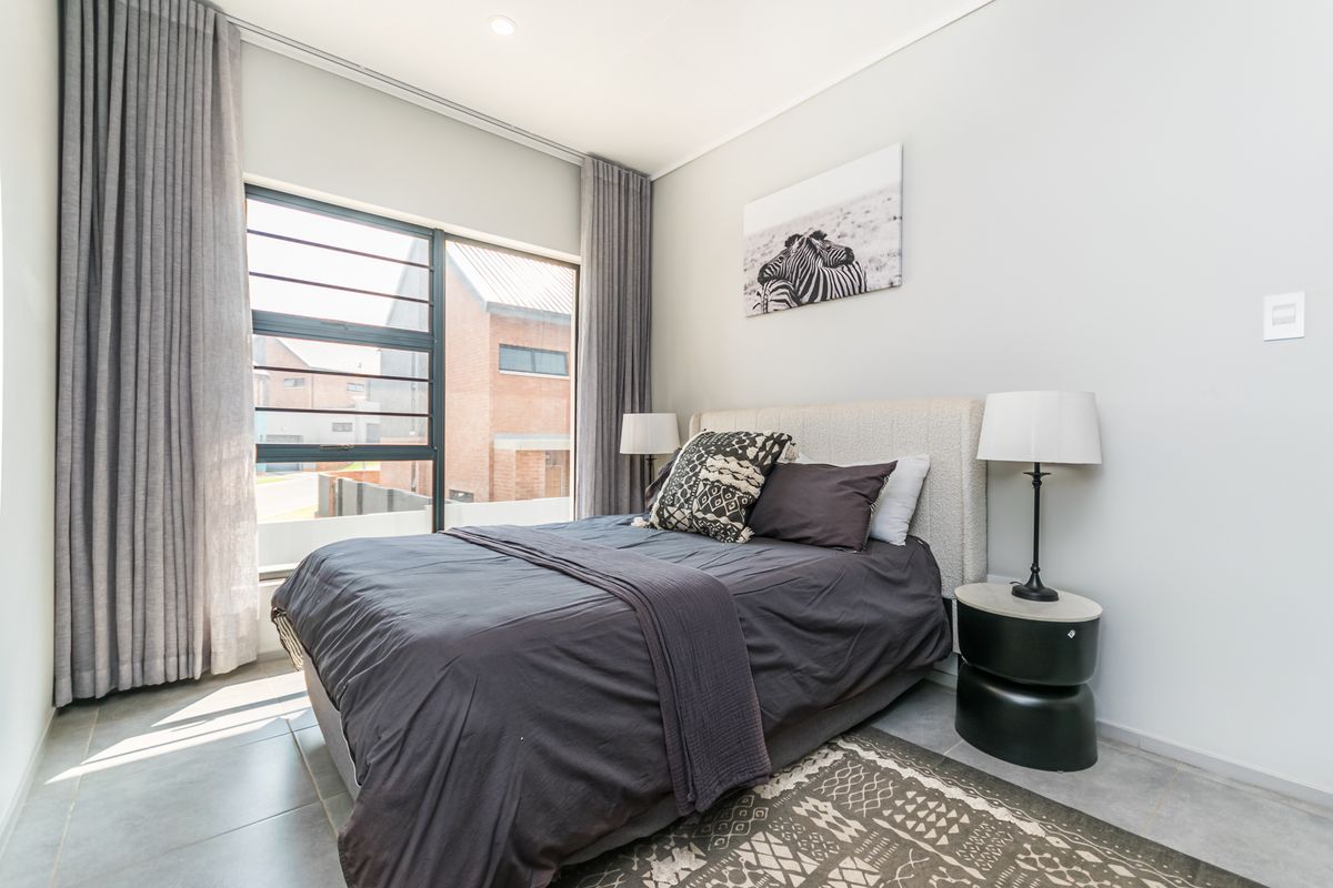 A modern, well-lit bedroom featuring large aluminium windows, neutral tiled flooring, and clean finishes, offering a comfortable and contemporary living space.