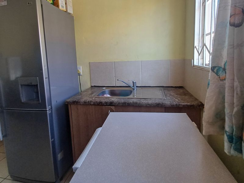 A compact kitchen area featuring a stainless steel sink, laminate countertop, and tiled splashback, with security bars installed on the window.