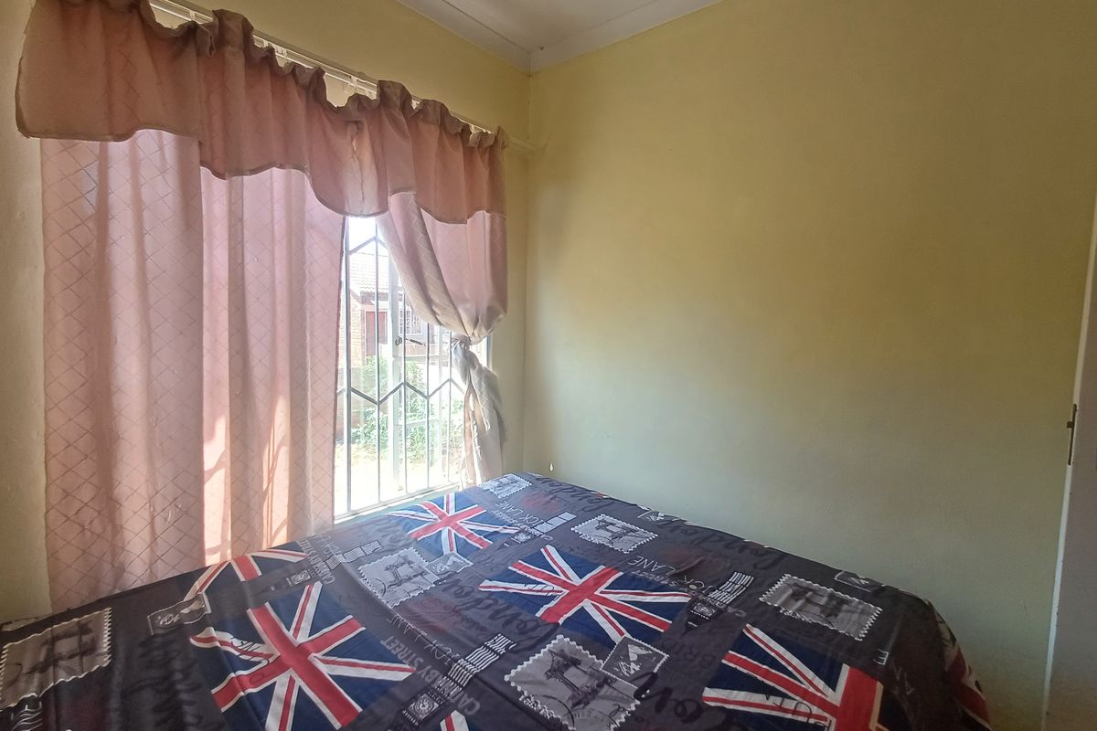A bedroom featuring security bars on the window and standard cornice detailing, currently showing signs of wear on the wall finishes.