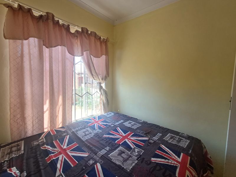 A bedroom featuring security bars on the window and standard cornice detailing, currently showing signs of wear on the wall finishes.