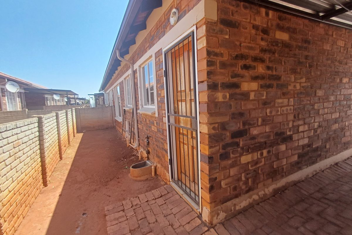 Rear exterior view of the townhouse featuring face brick construction, a security gate, paved walkway, and a private enclosed yard area.