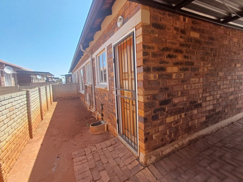 Rear exterior view of the townhouse featuring face brick construction, a security gate, paved walkway, and a private enclosed yard area.