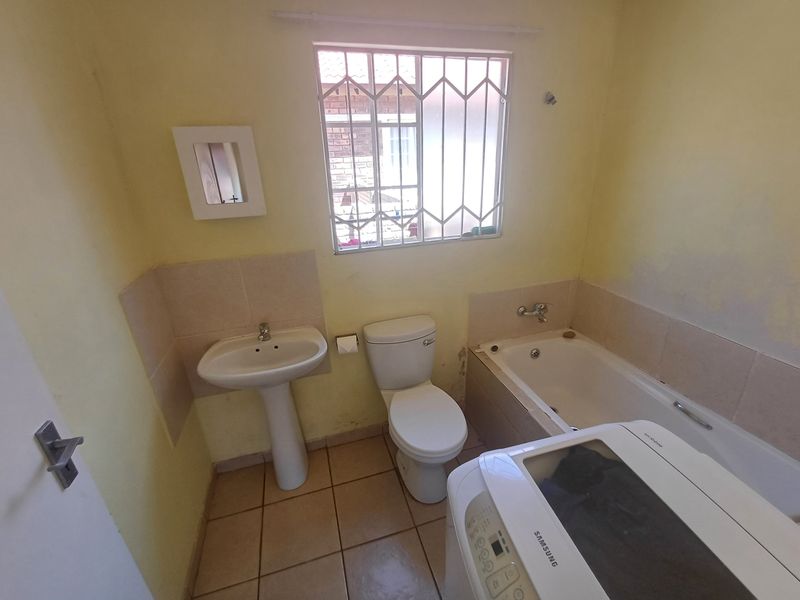 A functional bathroom featuring a pedestal basin, toilet, and bathtub with tiled splashbacks, requiring cosmetic updates to the wall finishes.