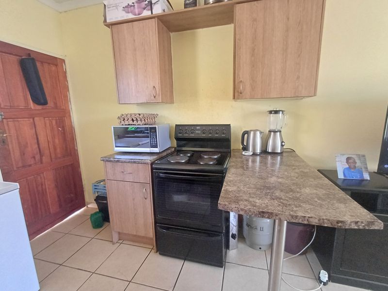 Compact kitchen area featuring laminate cabinetry, a freestanding stove, and tiled flooring, providing a functional space for meal preparation.
