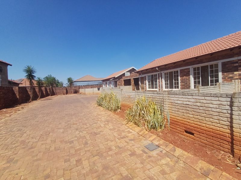Exterior view of a townhouse complex featuring face brick facades, tiled roofing, and a paved driveway with precast concrete boundary walls.