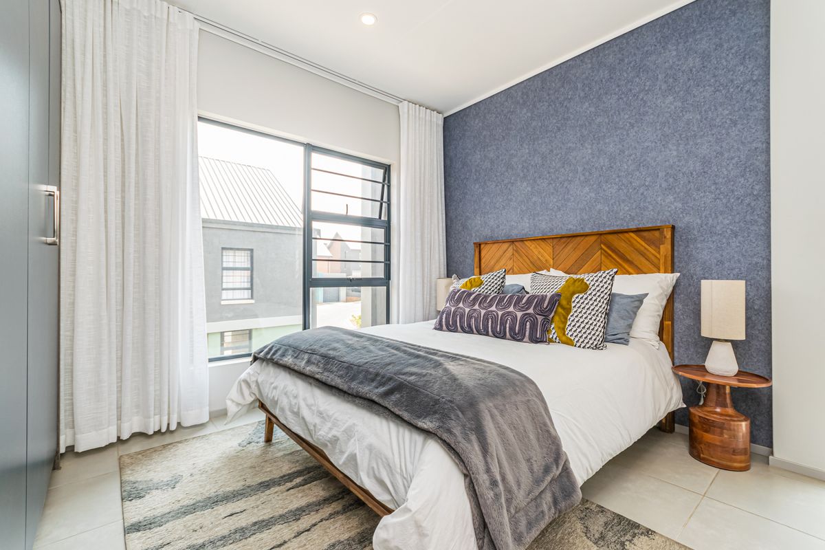A well-lit bedroom featuring a textured accent wall, large window with integrated louvers, and built-in cabinetry.