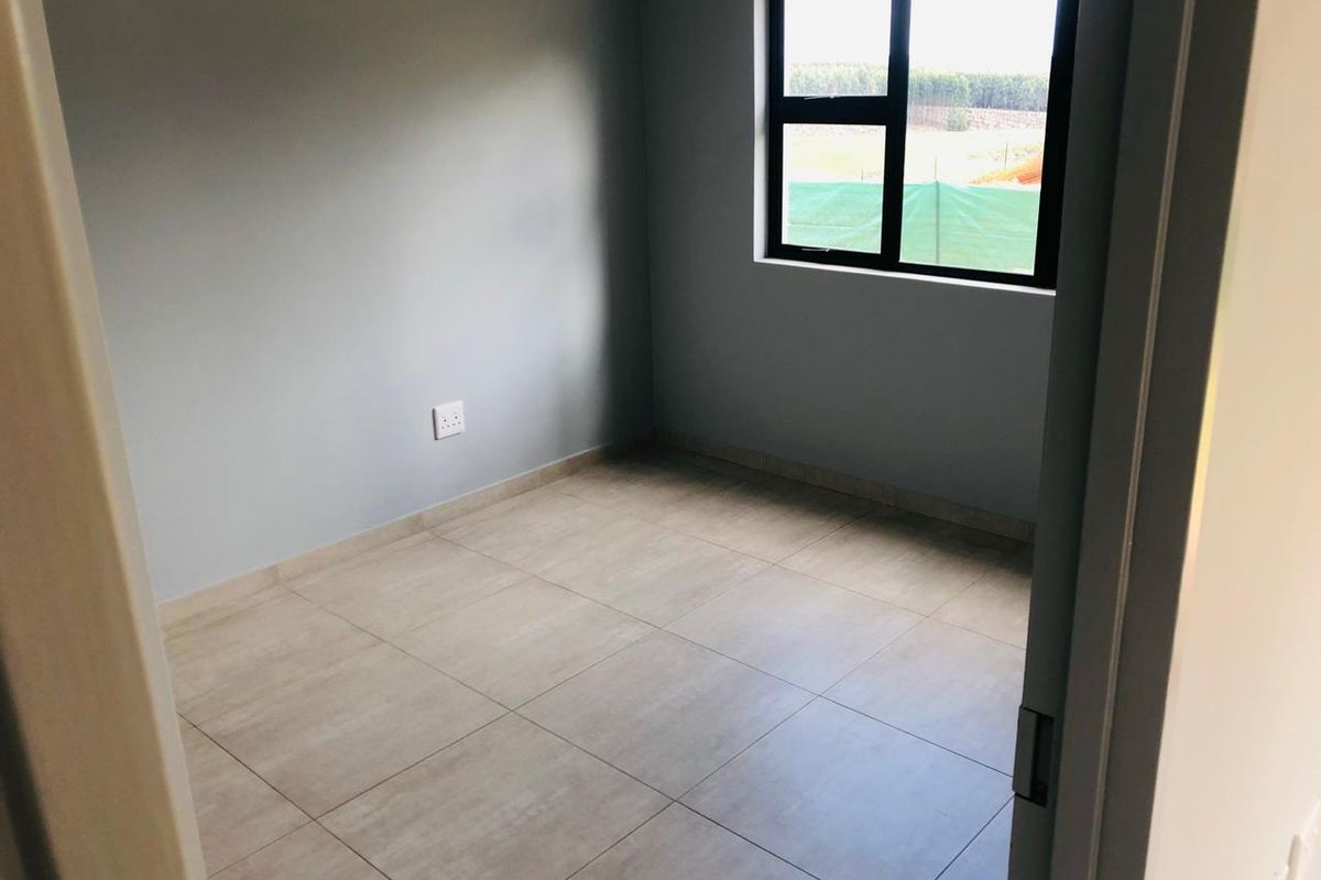 A clean, empty bedroom featuring neutral tiled flooring, grey walls, and a modern aluminium-framed window.