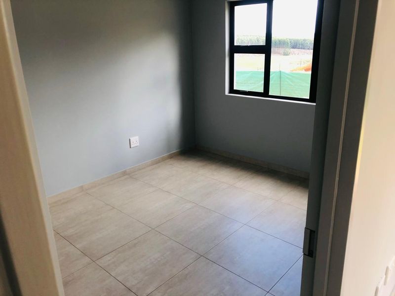 A clean, empty bedroom featuring neutral tiled flooring, grey walls, and a modern aluminium-framed window.