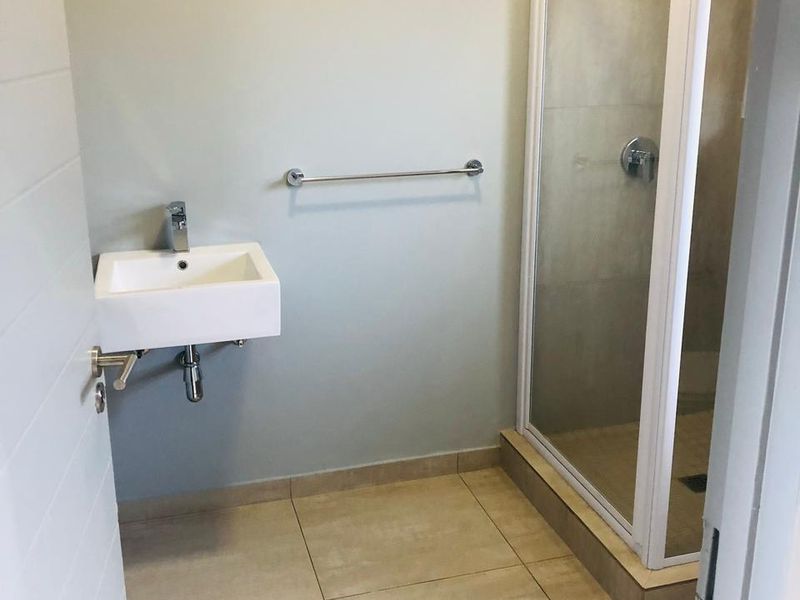 A clean, modern bathroom featuring a wall-mounted basin, a glass-enclosed shower, and neutral floor tiling.