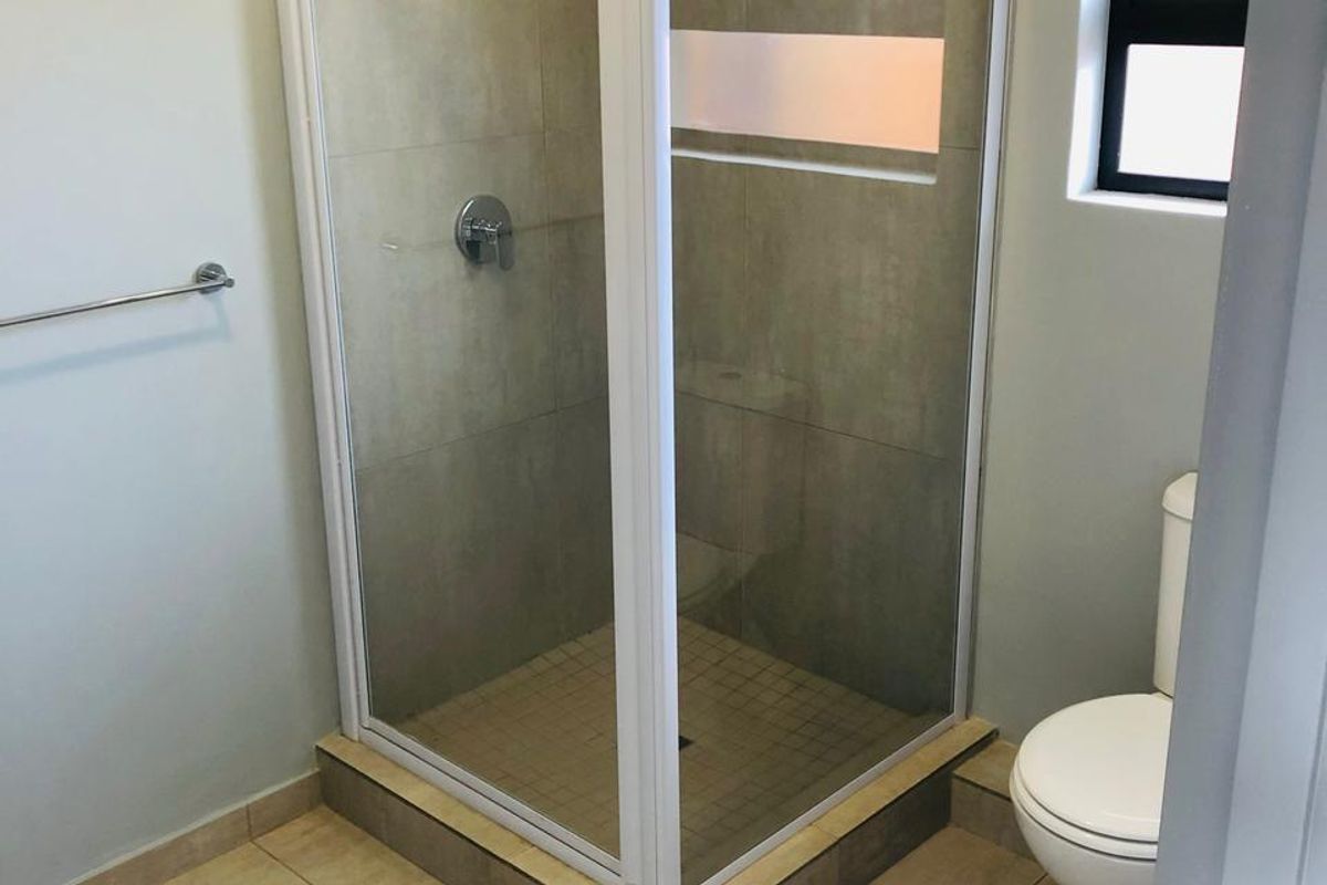 A clean, functional bathroom featuring a corner shower enclosure with tiled walls, a standard toilet, and neutral floor tiling.
