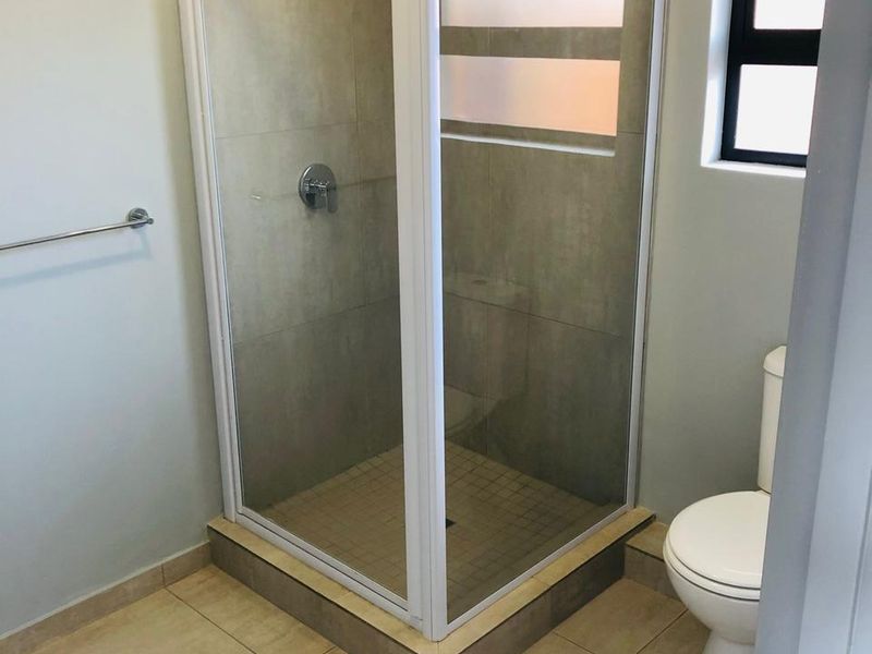 A clean, functional bathroom featuring a corner shower enclosure with tiled walls, a standard toilet, and neutral floor tiling.