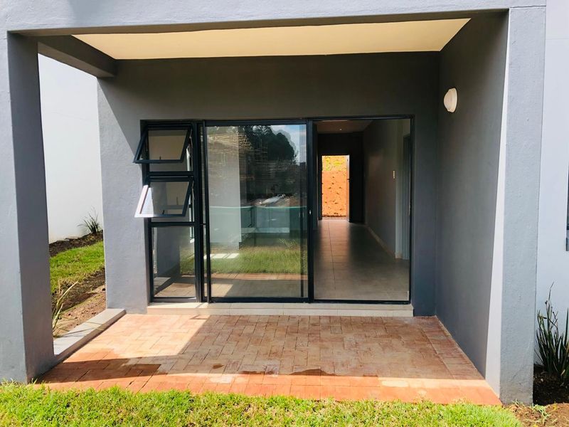 A covered patio area featuring brick paver flooring and a modern sliding glass door entrance into the apartment interior.