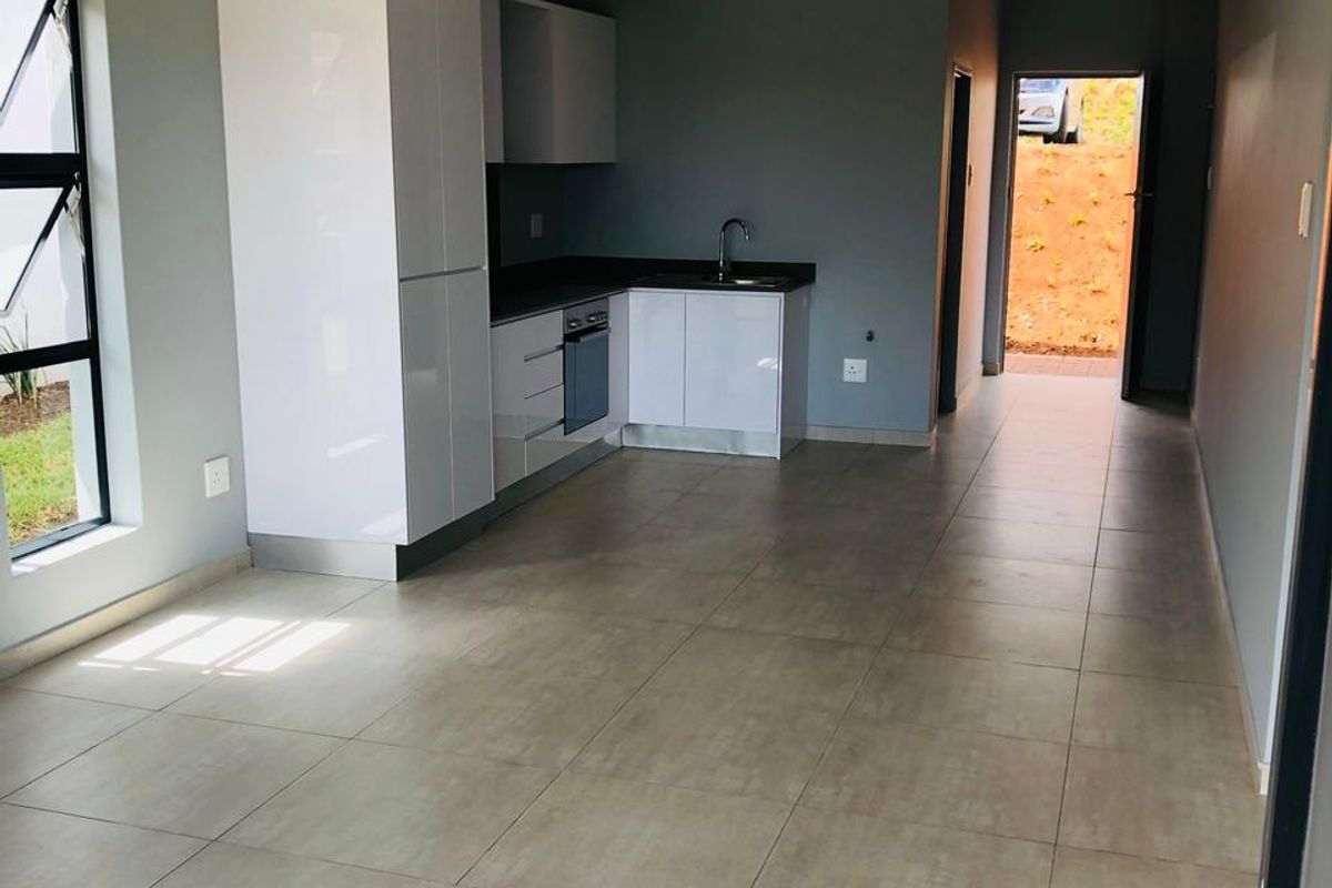 Modern open-plan kitchen and living area featuring sleek white cabinetry, integrated appliances, and neutral tiled flooring in a clean, vacant space.