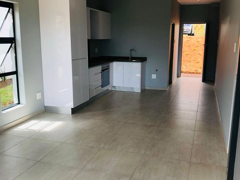 Modern open-plan kitchen and living area featuring sleek white cabinetry, integrated appliances, and neutral tiled flooring in a clean, vacant space.