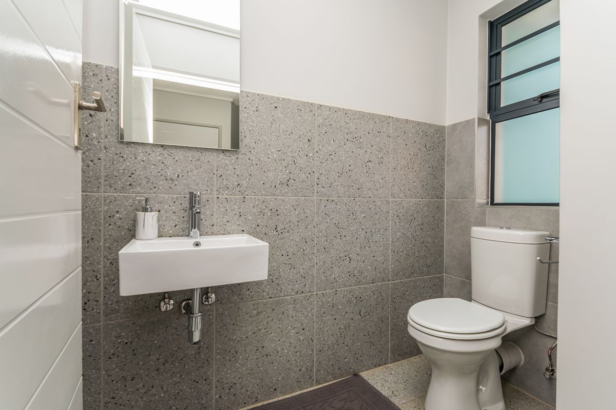 A modern, clean bathroom featuring a wall-mounted basin, chrome fixtures, and stylish terrazzo-style wall tiling with a frosted glass window.