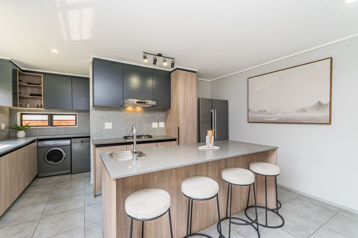 Modern kitchen featuring dark and wood-tone cabinetry, stone countertops, a central island with sink, and integrated gas hob with extractor fan.