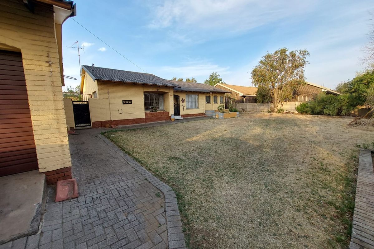 A view of the rear exterior of the house, featuring a brick facade, tiled roof, paved driveway, and a spacious garden area.
