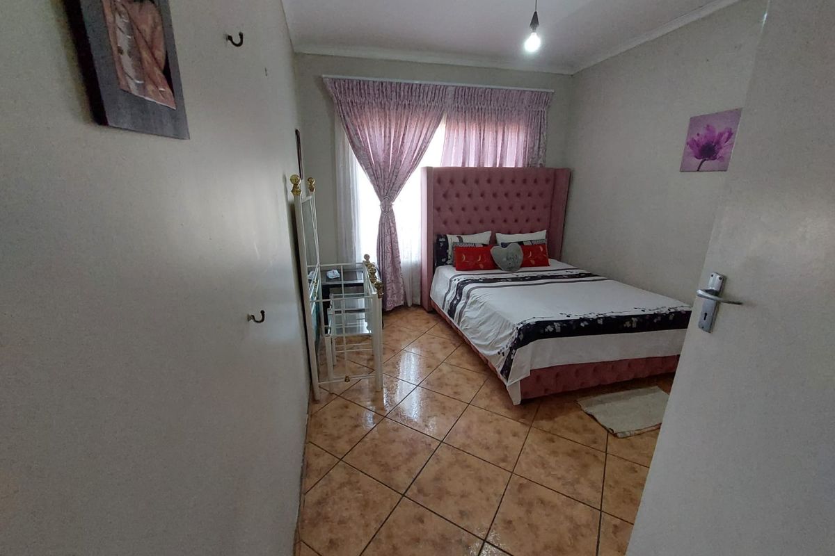 A bedroom featuring tiled flooring and natural light through window curtains.