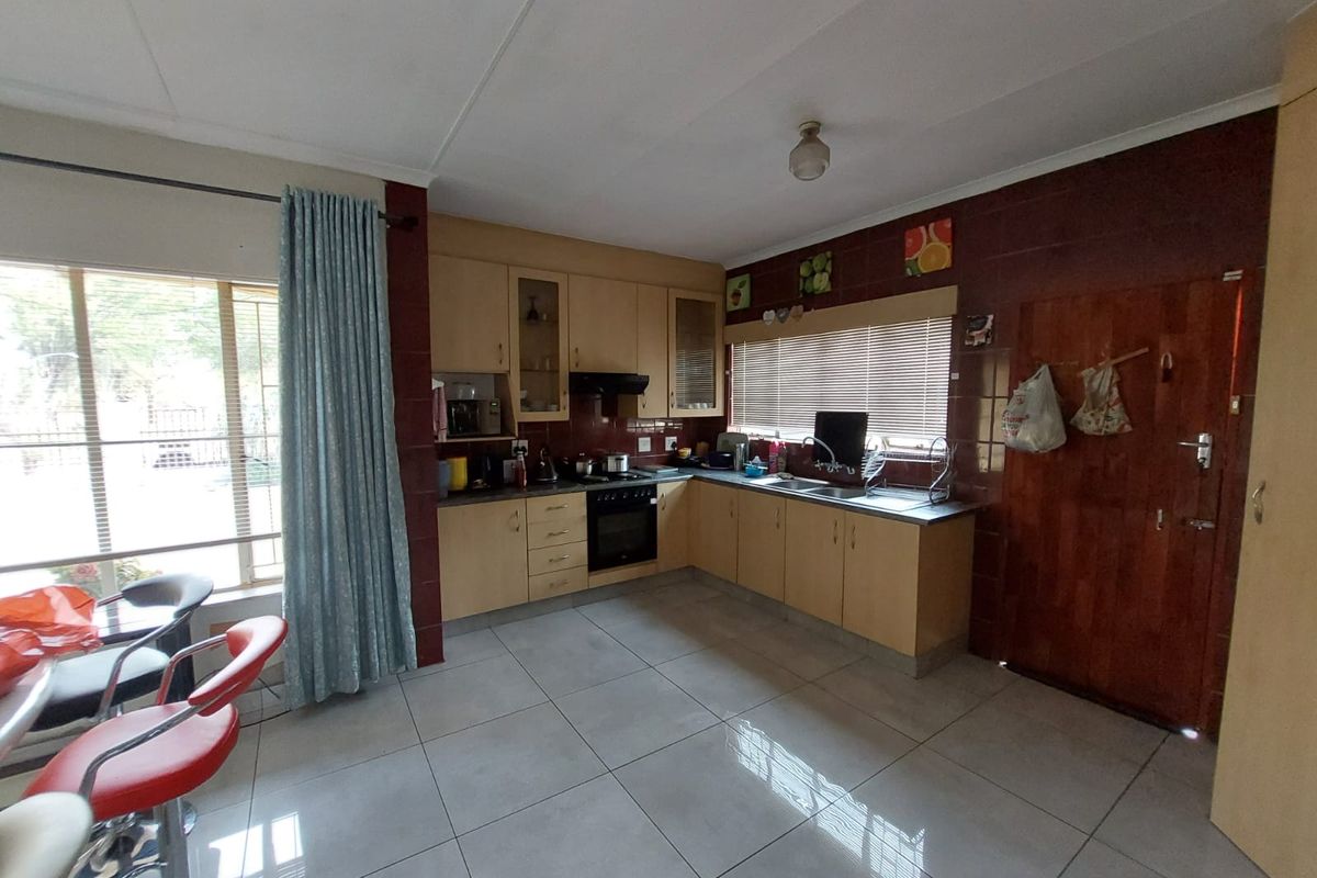 A functional kitchen featuring light wood cabinetry, tiled flooring, built-in oven and hob, and ample natural light from large windows.