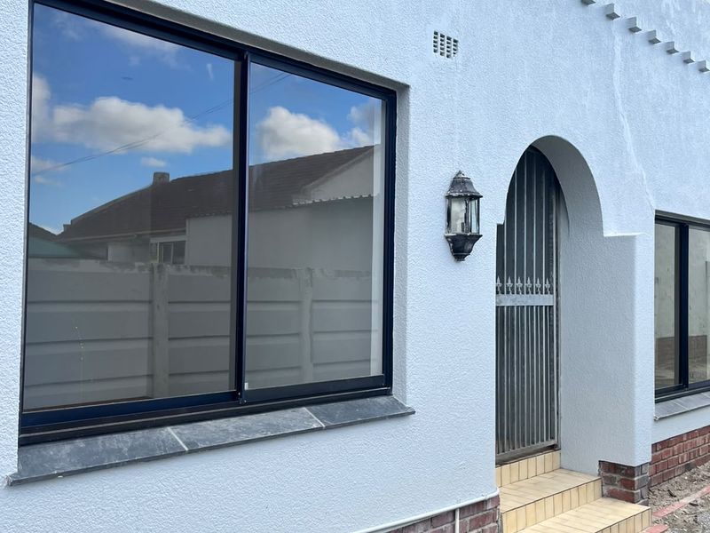 Front facade featuring an arched entrance, security gate, and modern aluminium sliding windows with a brick base.