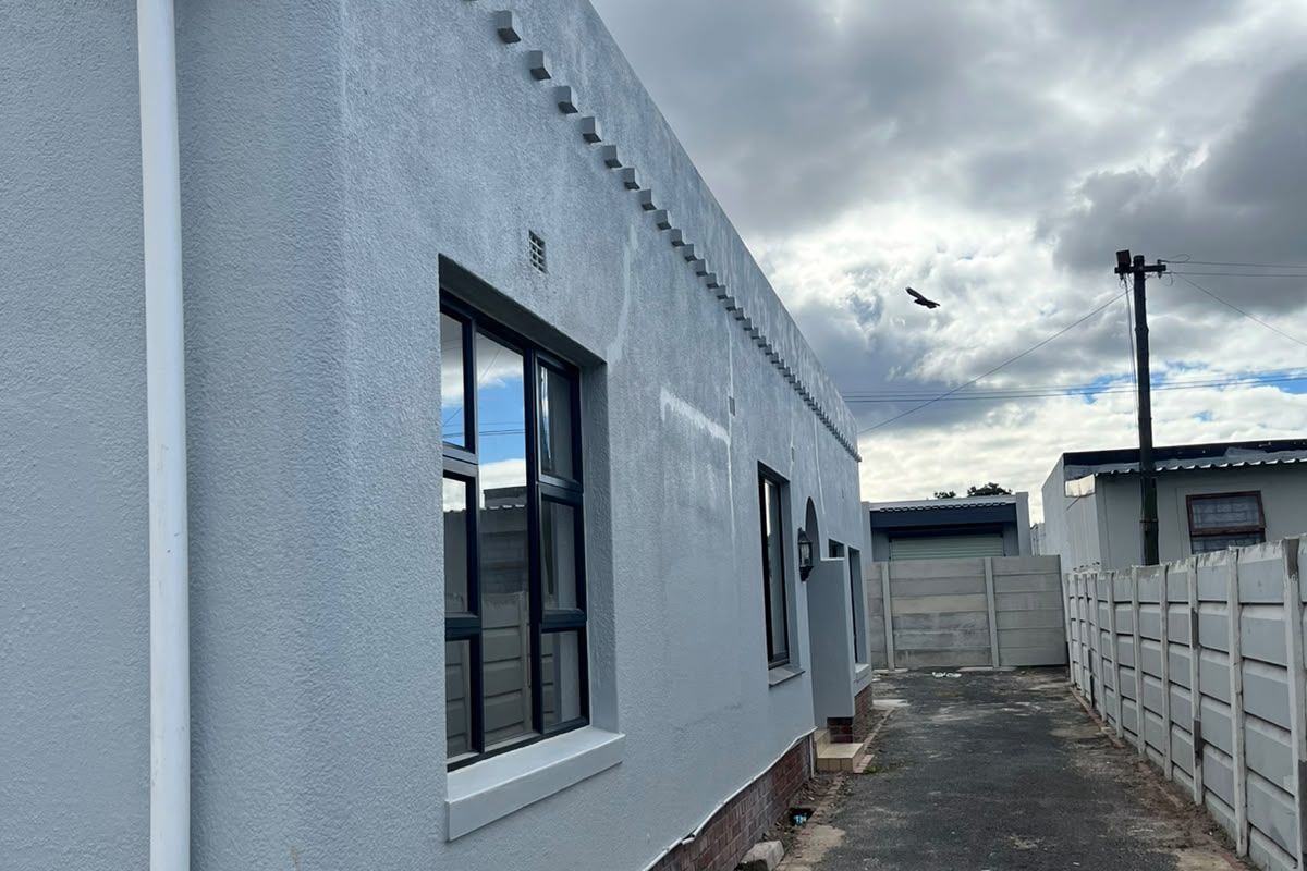 Side view of the property showing the exterior wall, aluminium window frames, and a paved driveway leading to the rear boundary wall.