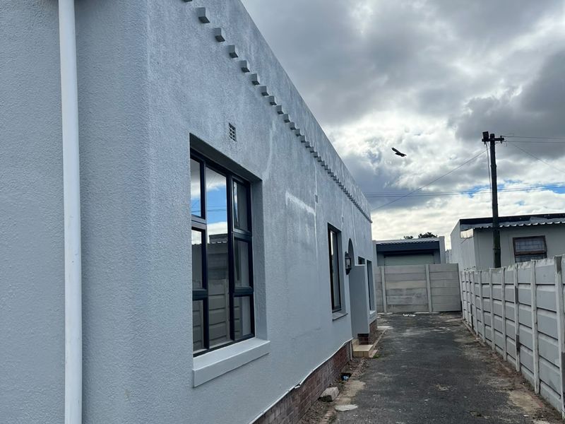 Side view of the property showing the exterior wall, aluminium window frames, and a paved driveway leading to the rear boundary wall.