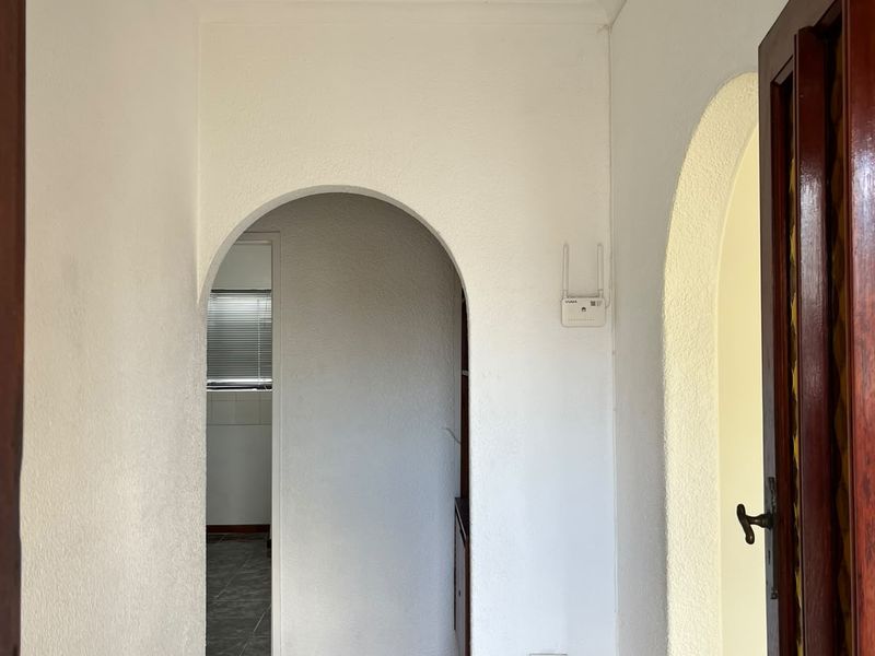 A bright, empty hallway featuring arched doorways, neutral tiled flooring, and clean white walls, providing a clear transition between living spaces.