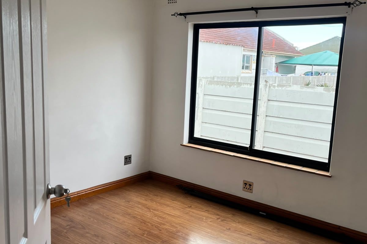 A bright, empty bedroom featuring laminate flooring, recessed downlights, and a modern black aluminium sliding window.