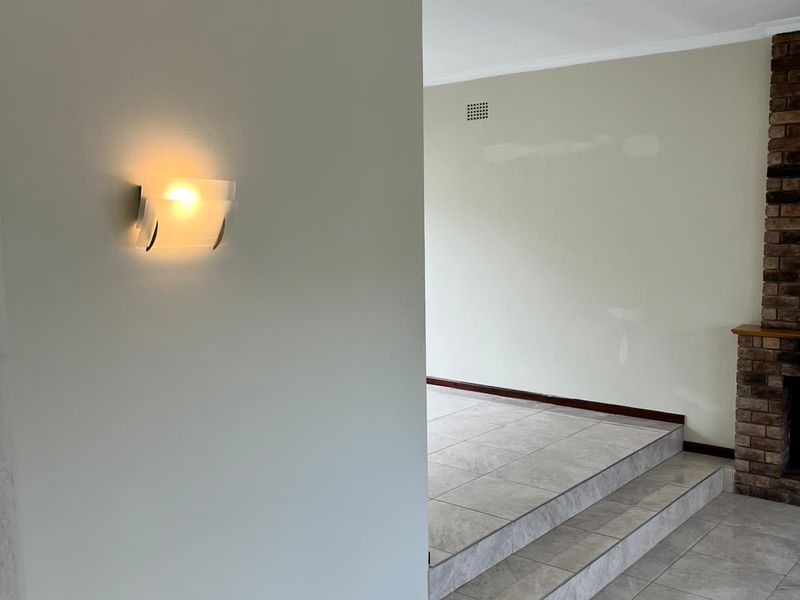 An empty living area featuring a brick fireplace, tiled flooring, and a raised floor section, finished with neutral wall paint and cove cornicing.