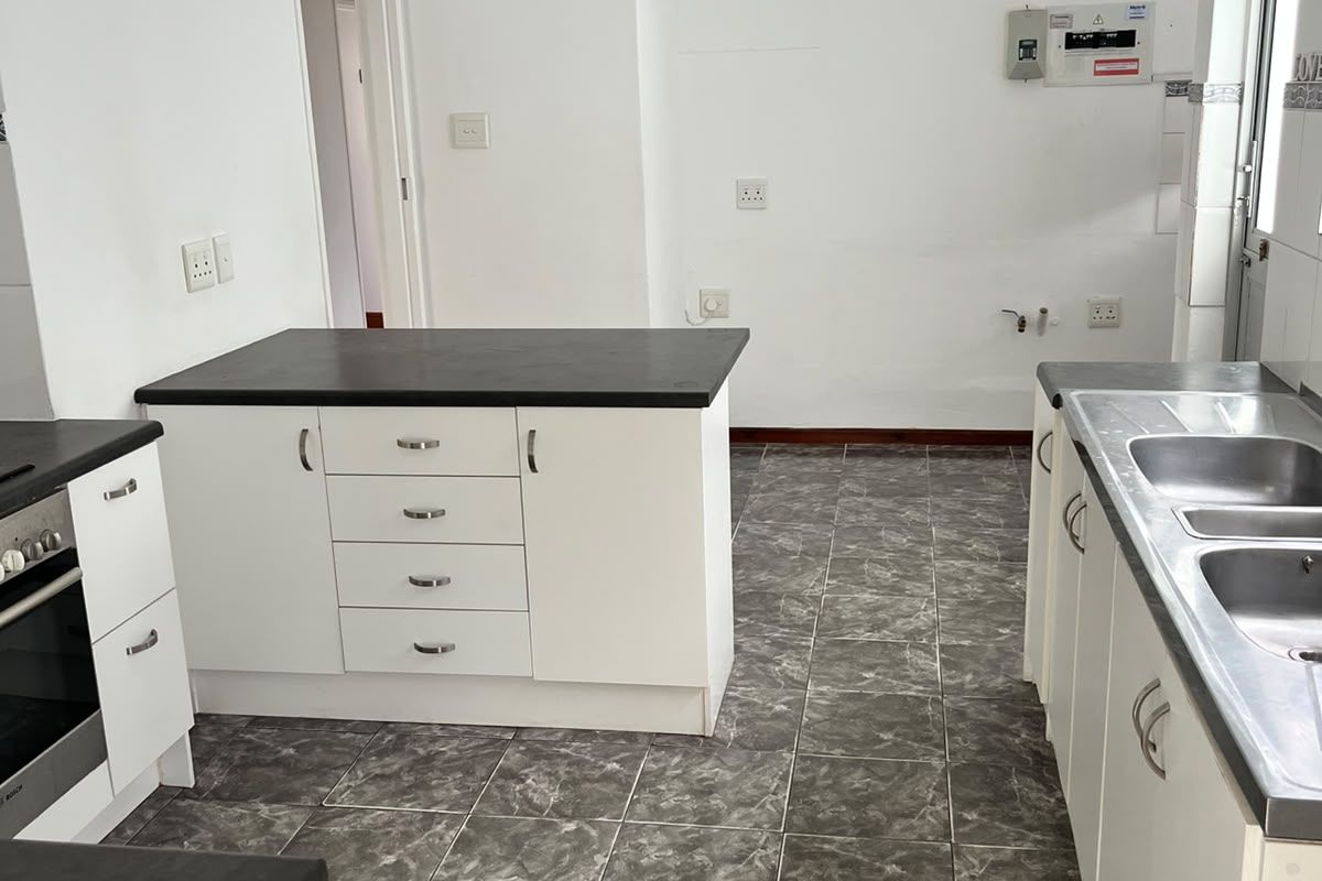 A functional kitchen featuring white cabinetry, dark laminate countertops, tiled flooring, a built-in oven, and a double stainless steel sink.