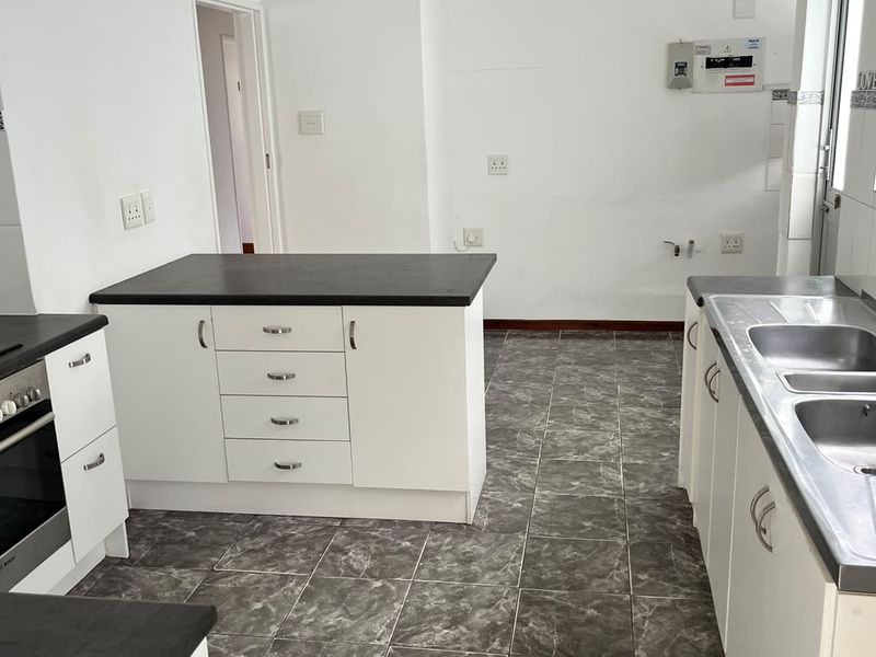 A functional kitchen featuring white cabinetry, dark laminate countertops, tiled flooring, a built-in oven, and a double stainless steel sink.
