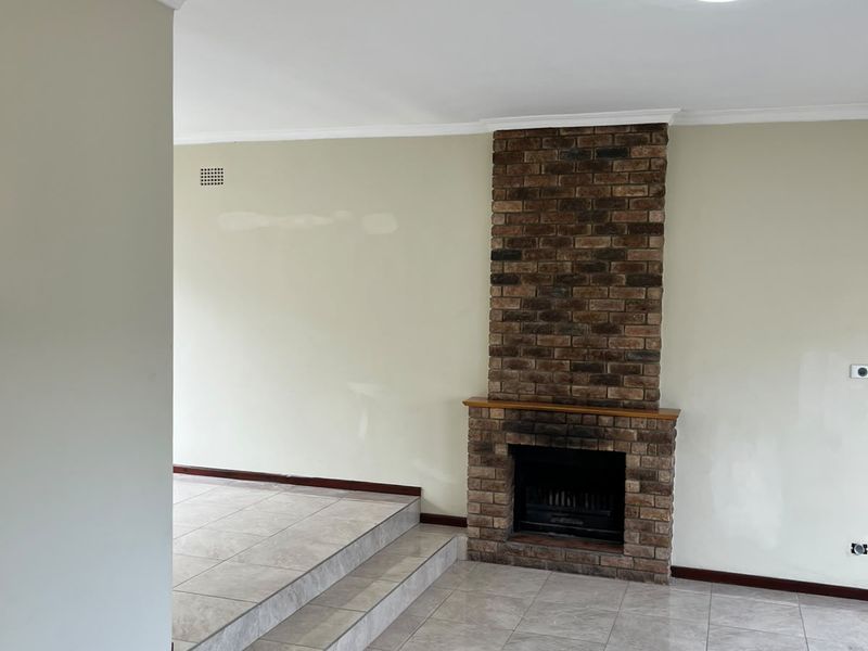 An empty living room featuring a prominent brick fireplace, tiled flooring, and a raised platform area, ready for personalization.