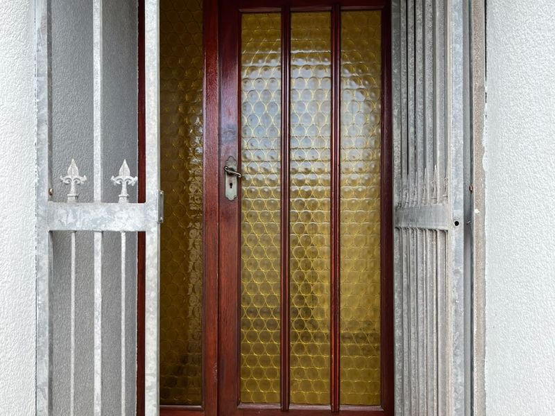 A secure residential entrance featuring an arched doorway, a metal security gate, and a classic timber front door with textured glass panels.