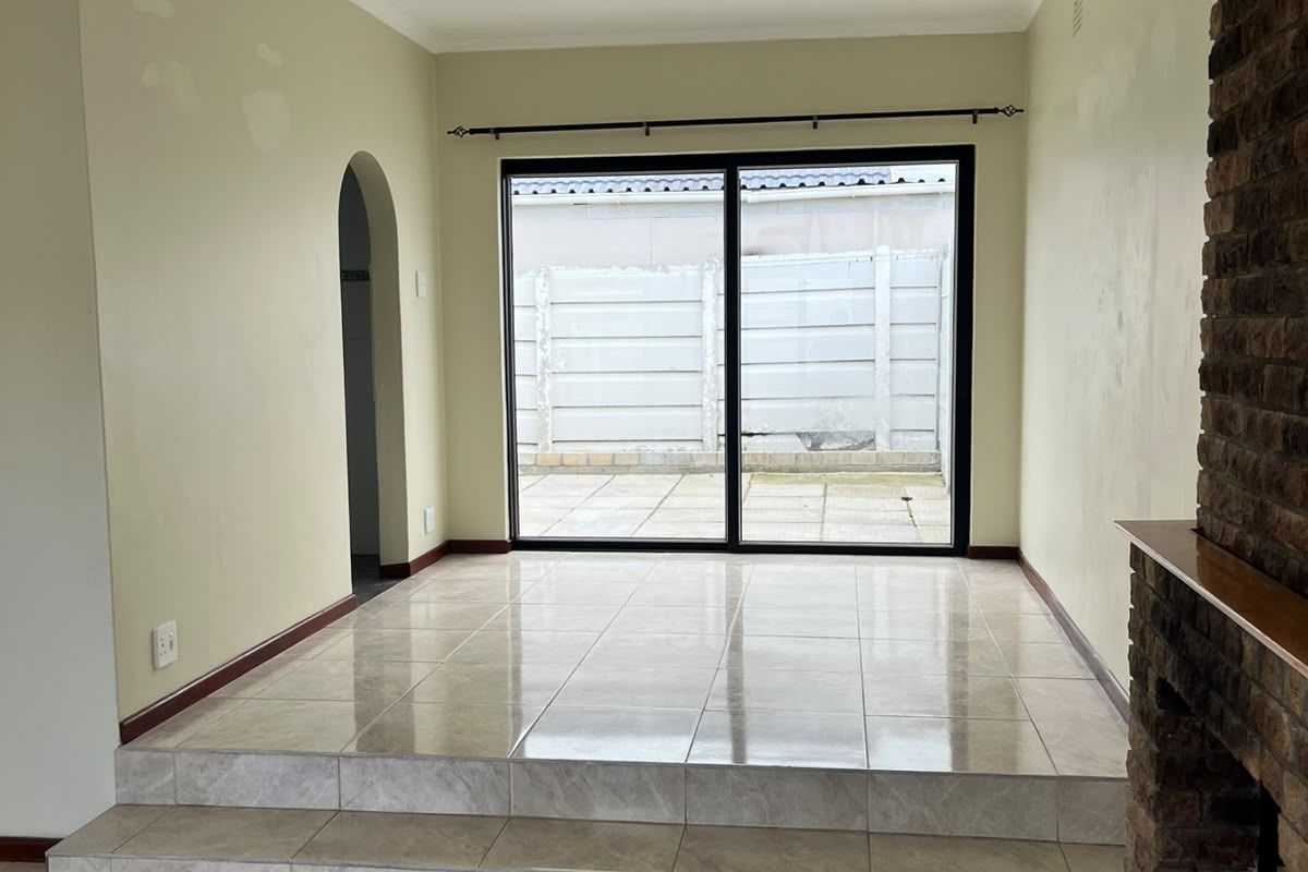 Spacious living area featuring a raised tiled platform, a classic brick fireplace, and sliding glass doors leading to the rear patio.