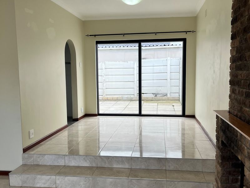 Spacious living area featuring a raised tiled platform, a classic brick fireplace, and sliding glass doors leading to the rear patio.