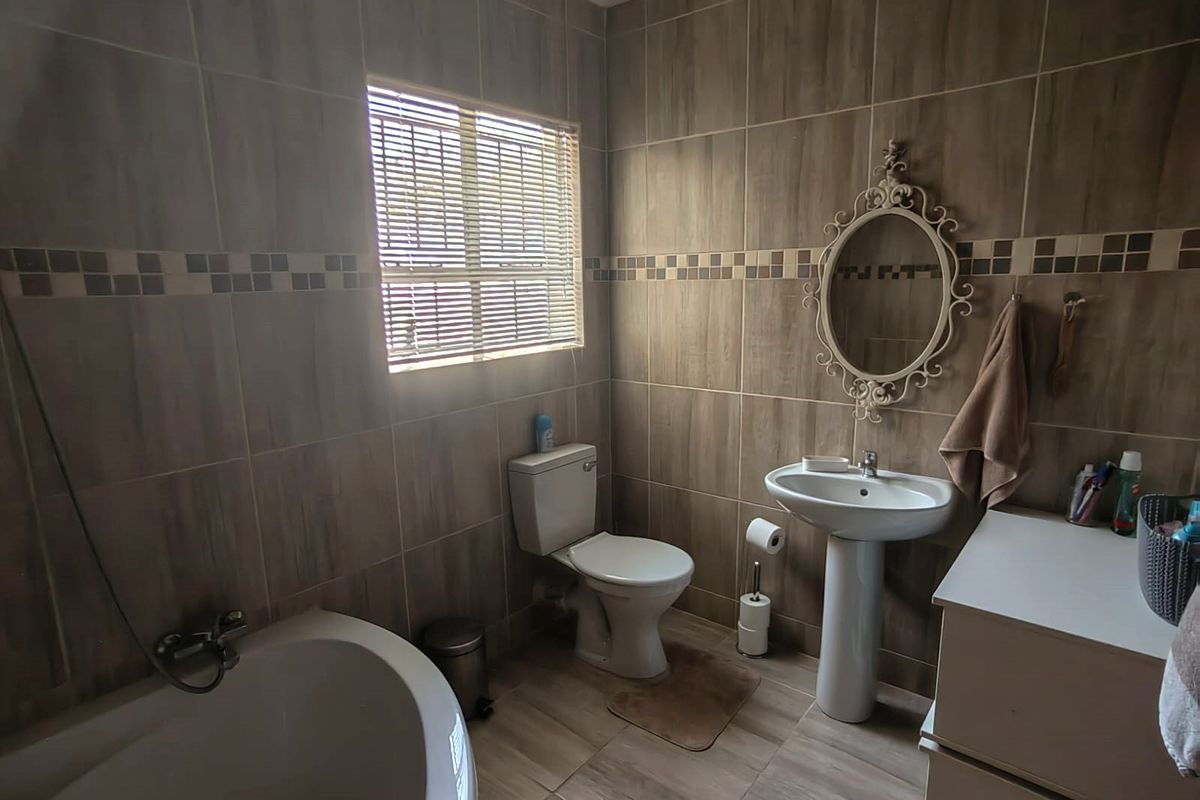 A functional bathroom featuring full-height wall tiling, a pedestal basin, a toilet, and a bathtub with neutral earth-toned finishes.