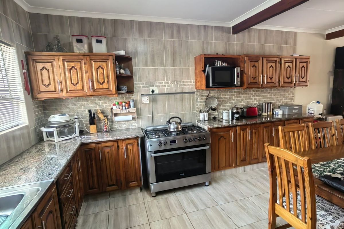 A functional kitchen featuring wooden cabinetry, granite countertops, a gas stove, and tiled finishes, offering a classic aesthetic with ample storage space.