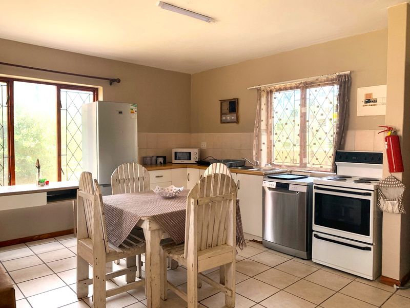 Open-plan kitchen and dining area featuring tiled flooring, functional cabinetry, and large windows with security bars, offering a practical layout for daily living.