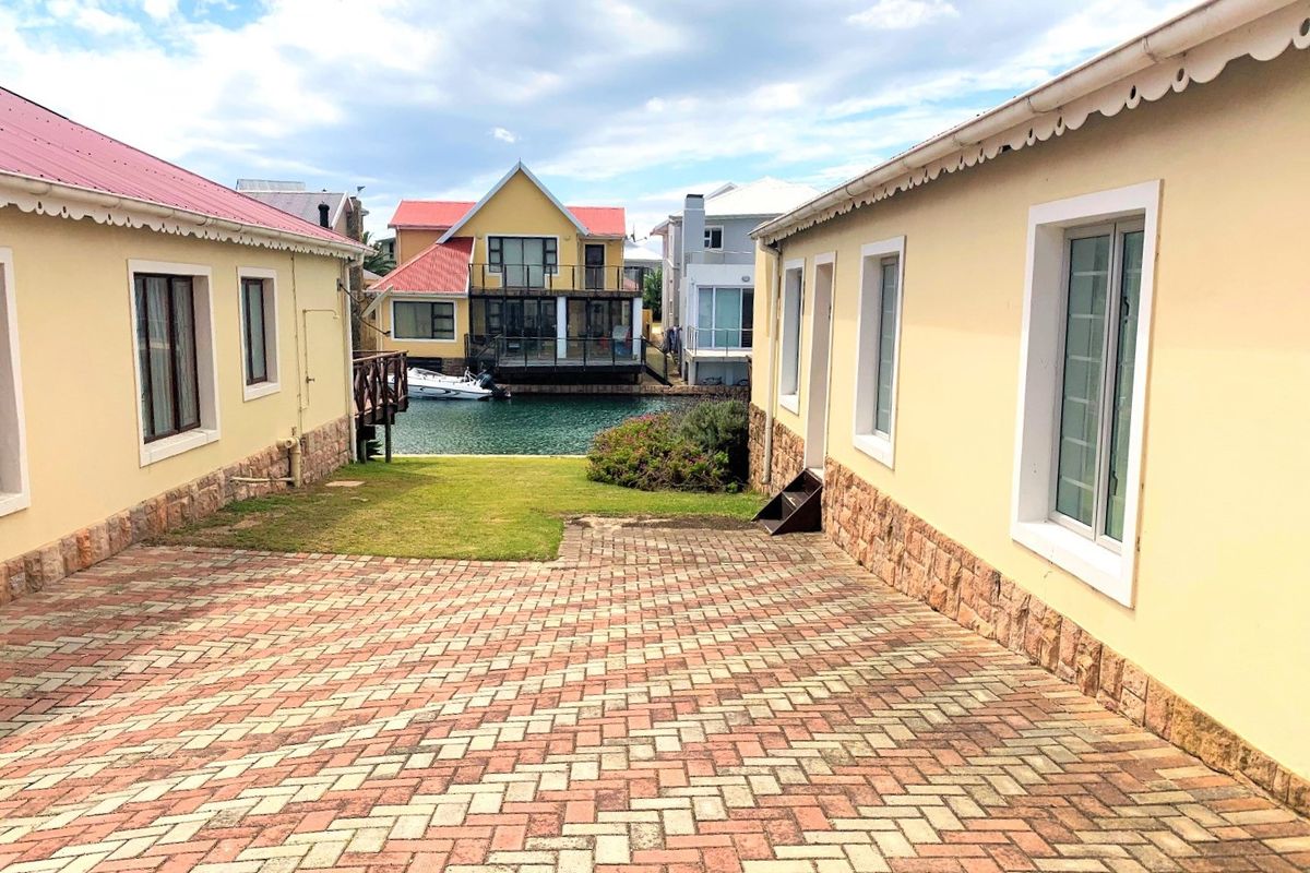 A view of the rear exterior area featuring paved driveway, stone-clad walls, and access to the waterfront canal.