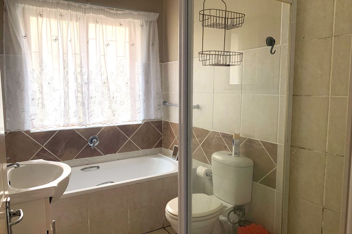 A functional bathroom featuring a bathtub, separate shower enclosure, toilet, and pedestal basin with neutral wall tiling.