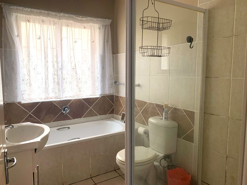 A functional bathroom featuring a bathtub, separate shower enclosure, toilet, and pedestal basin with neutral wall tiling.