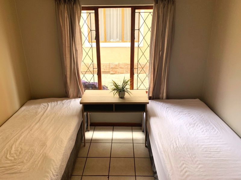 A bedroom featuring tiled flooring and a window with security bars, providing natural light and a view of the exterior area.
