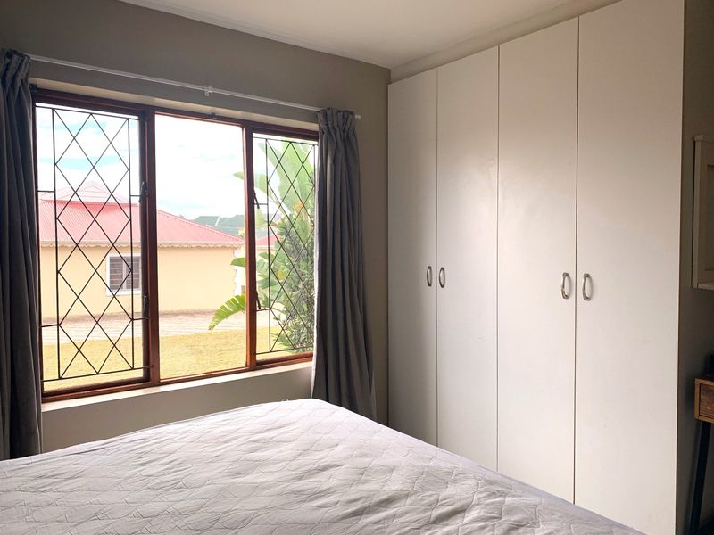 A bedroom featuring built-in cupboards and a window with security bars, offering a view of the surrounding residential area.