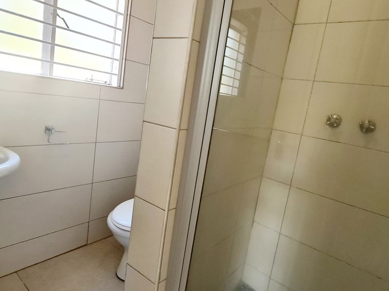 A functional bathroom featuring a pedestal basin, toilet, and a glass-enclosed shower with tiled walls and security bars on the window.