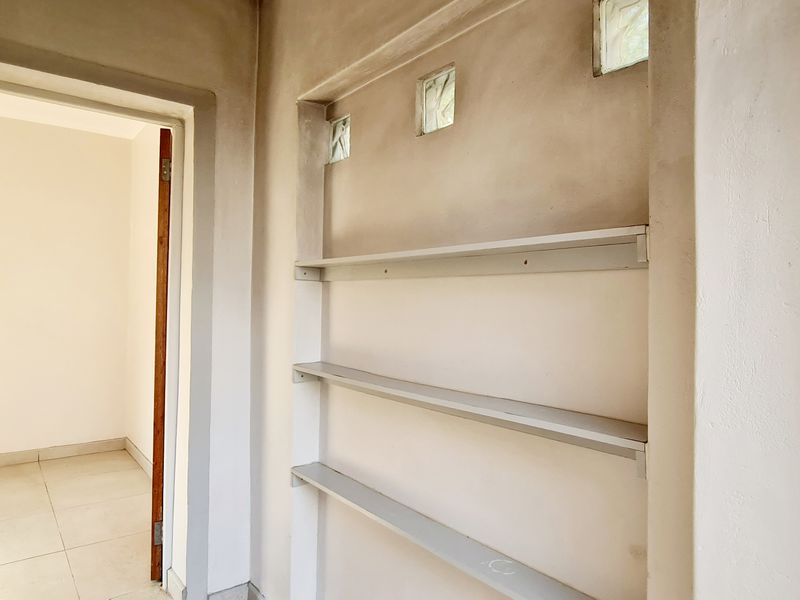 A hallway area featuring built-in shelving and glass block wall inserts, currently in an unfinished state requiring cosmetic completion.