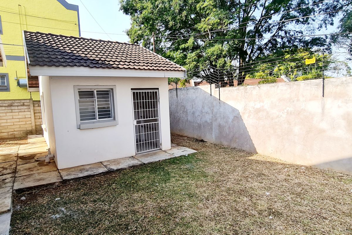 Rear exterior view of the townhouse featuring a small outbuilding, paved walkway, and perimeter wall with electric fencing.