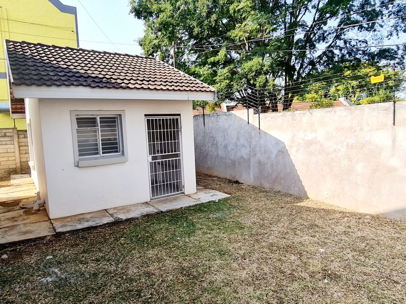 Rear exterior view of the townhouse featuring a small outbuilding, paved walkway, and perimeter wall with electric fencing.