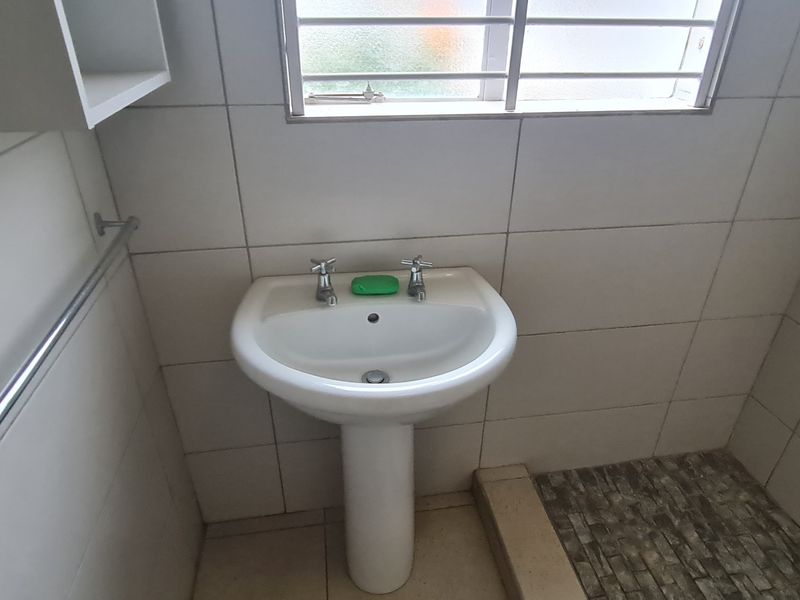 A compact bathroom featuring a pedestal basin, tiled walls, and a window with security bars. The space requires cosmetic updates to improve its condition.